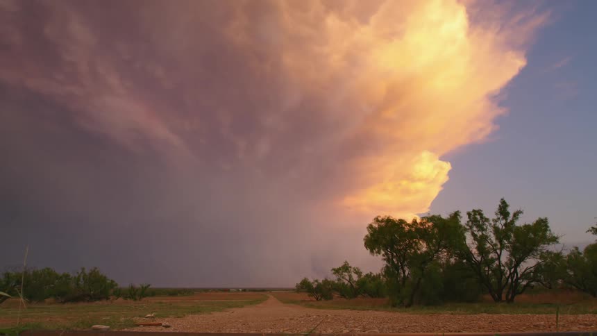 Looking down a rural dirt road at an intense severe thunderstorm at sunset at lightning strikes within the storm system and illuminates the purple part of the cloud