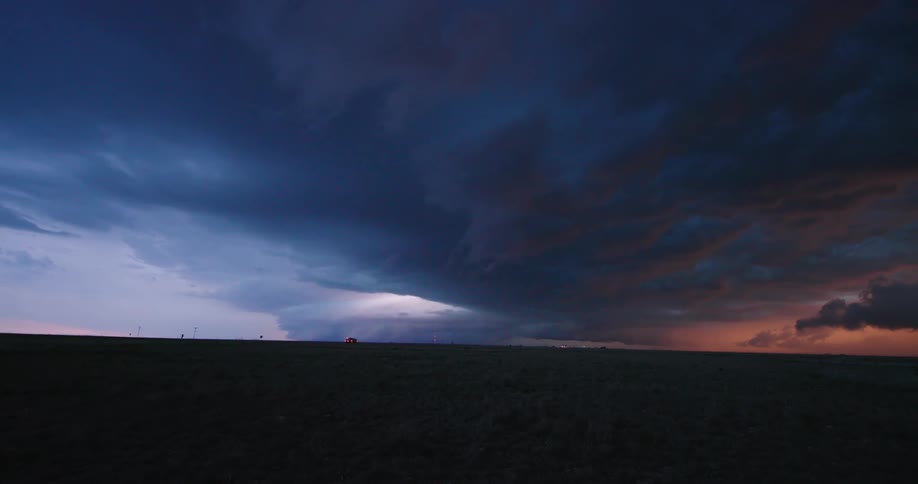 Super wide real time shot of a vast supercell severe thunderstorm building and roiling across the New Mexico desert after the sun has set as semi trucks lumbar down the interstate and lightning flashes