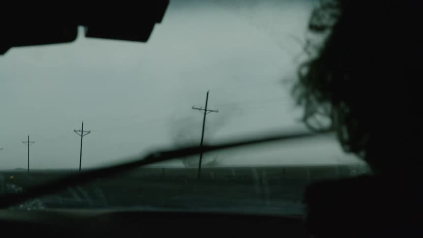 Real time shot looking through the windshield at a dust devil small tornado as a man points his finger at it