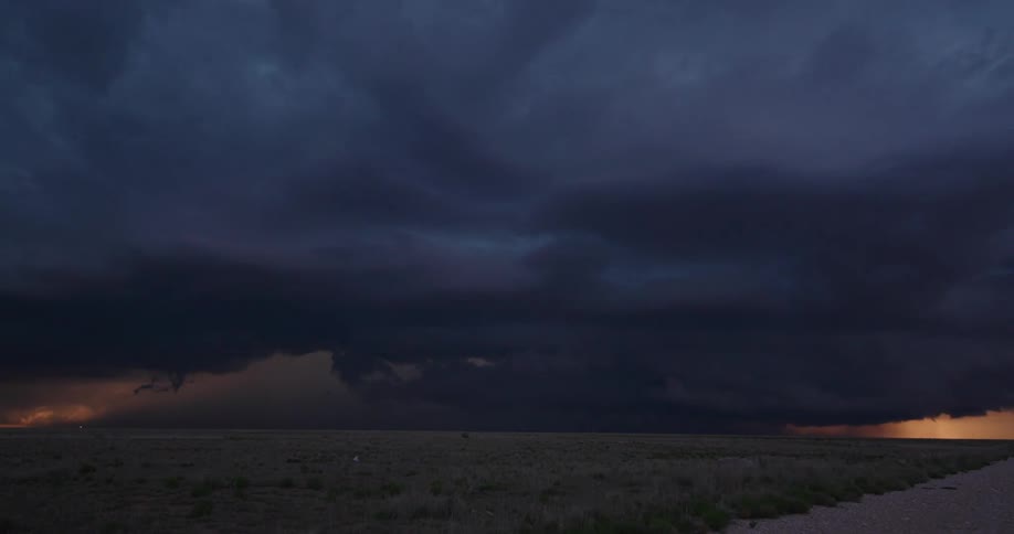 Super wide time lapse shot of an intense and overwhelming super cell storm that pushes straight towards and overwhelms the camera transitioning from golden light to dark purple tones