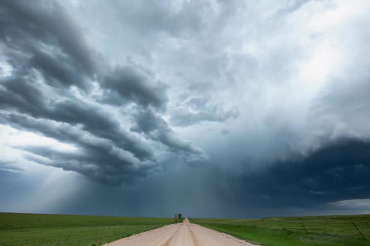 Time lapse of a severe thunderstorm blowing away from camera with a rural dirt road center frame on the bottom of the horizon line