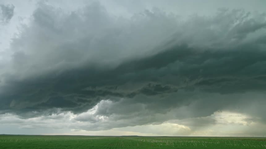 Time lapse of rolling storm clouds rapidly pushing straight towards camera over a green alfalfa fields in springtime
