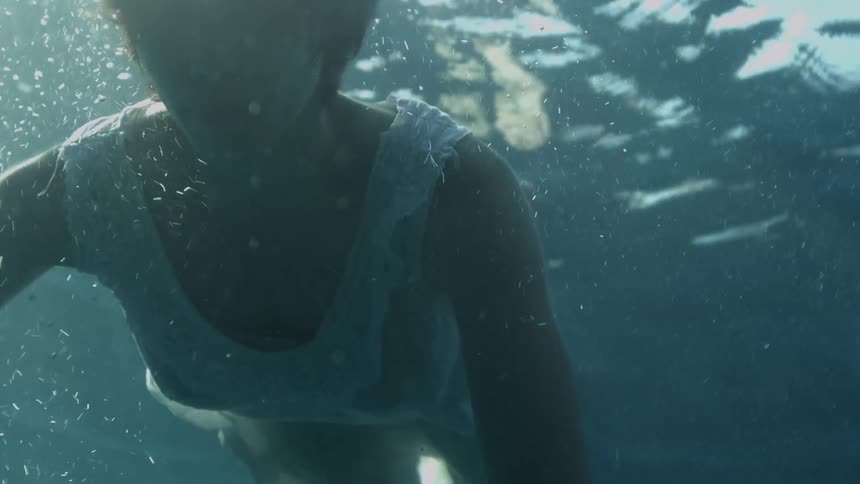 Depressed woman with short hair and a white dress floats underwater