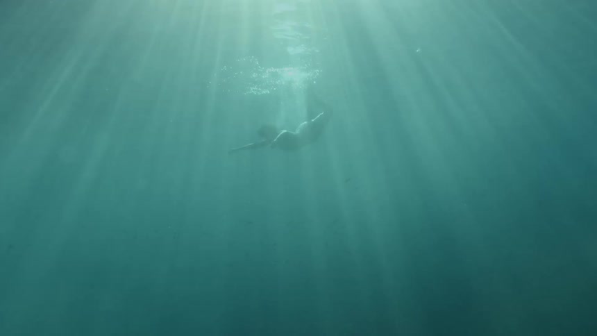 Sunlight shining down on a person suspended in deep ocean water