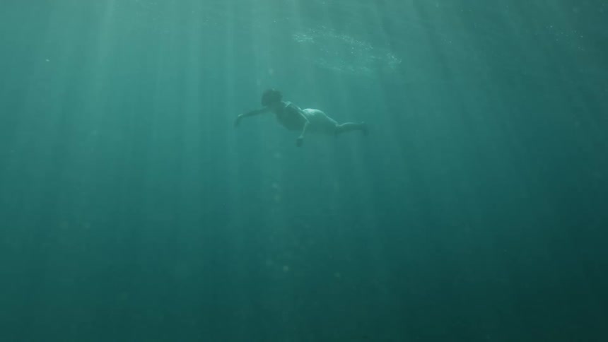 A woman swims underwater in a white dress and spreads her arms out