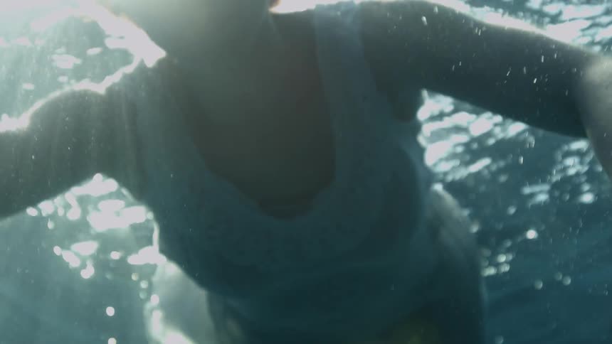 Depressed woman with short hair and a white dress floats underwater