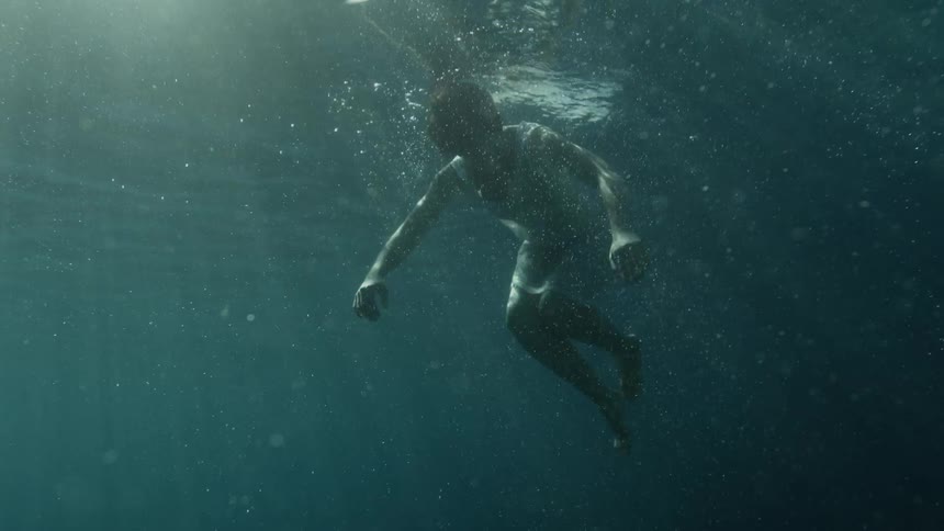 A person floats underwater looking lifeless as sun streams through the surface