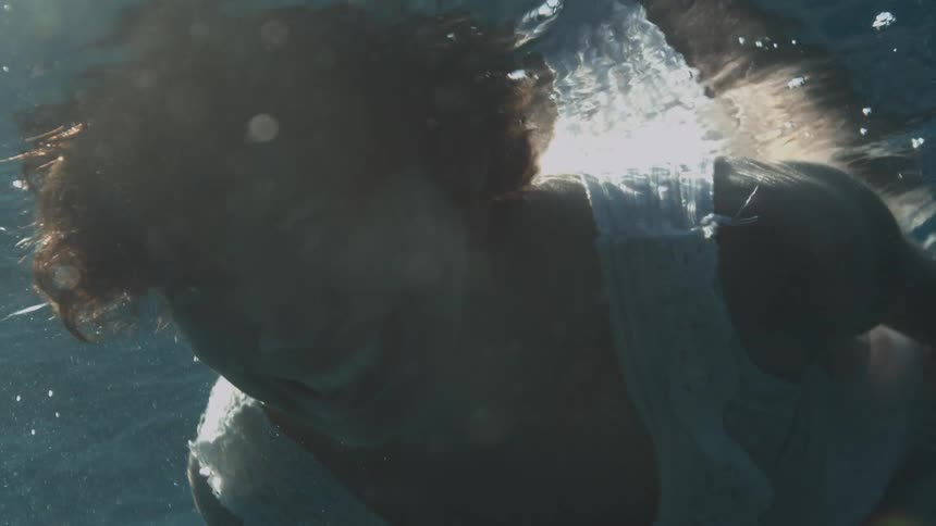 Woman with short hair and a white dress cries and screams underwater