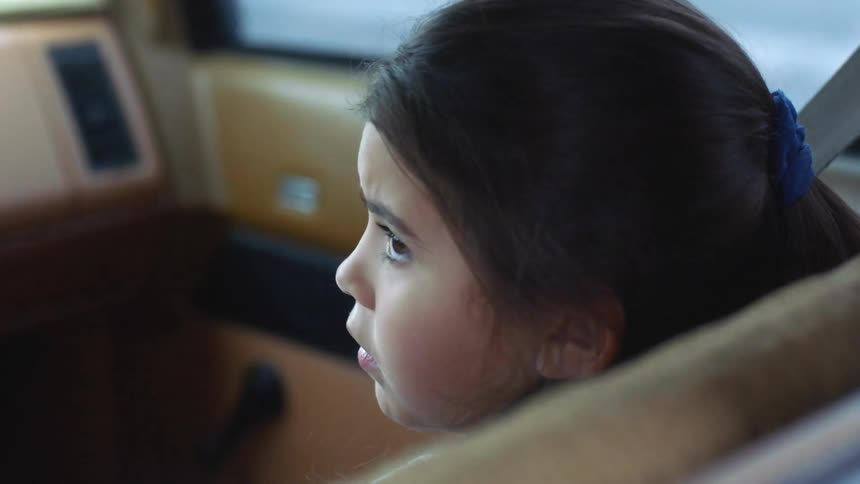 Little girl with dark hair sits in the seat of a moving car
