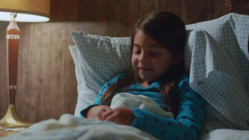 A little girl in her pajamas is settling into bed under her blanket