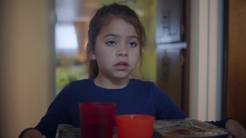 Little girl holding a tray with tv dinners looking onwards scared