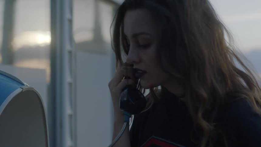 A woman looks frustrated and disappointed as she talks outside on a pay phone