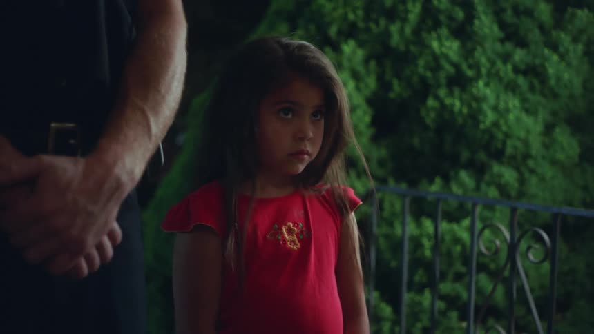 A person opens a door as a man and a little girl stand outside with trees in the background