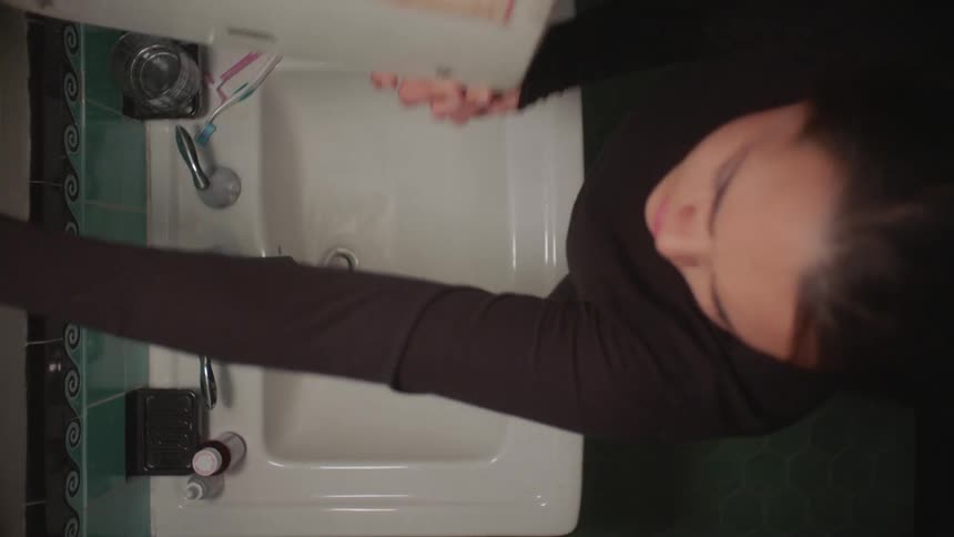 A woman removes a prescription pill bottle from her bathroom cabinet
