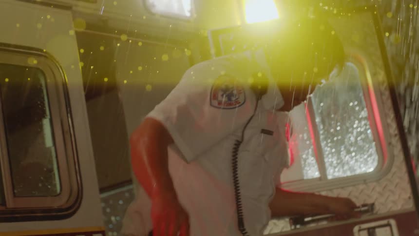 A middleaged male emt steps unevenly out of an ambulances back door into the night during a heavy lightning storm
