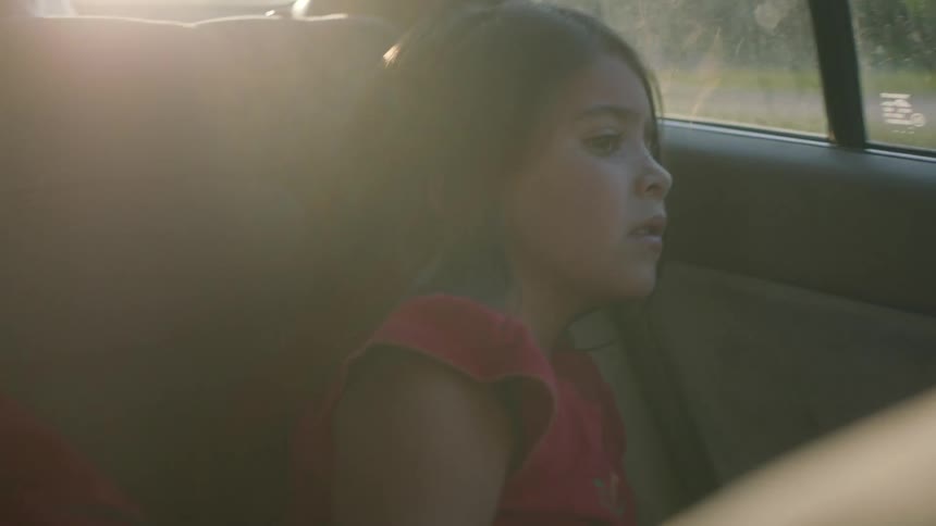 Little girl sitting in the backseat of a moving vehicle looking out the window