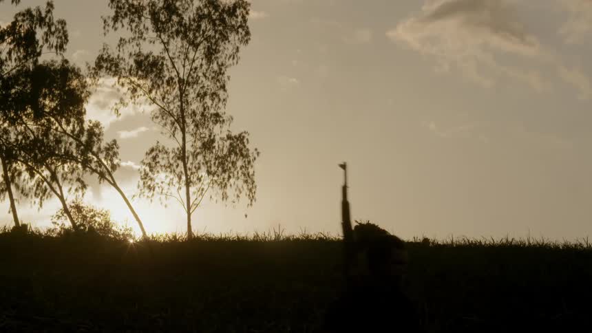 Armed men walking through a rural area at sunrise