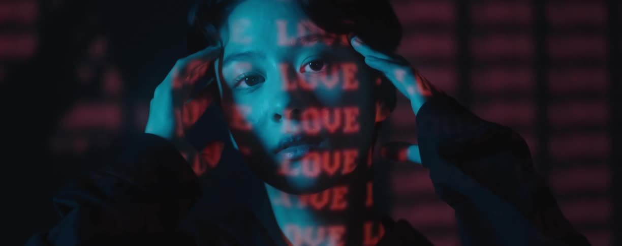 A woman poses in a dark room with red text projected to her face and the wall behind