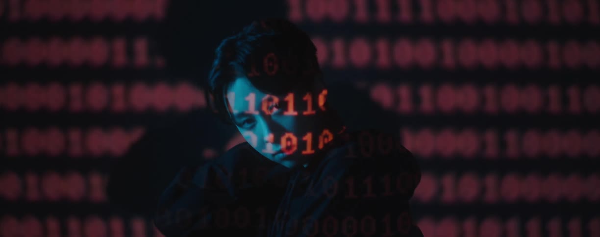 Binary code is flashed on a models face as she stands in front of a screen
