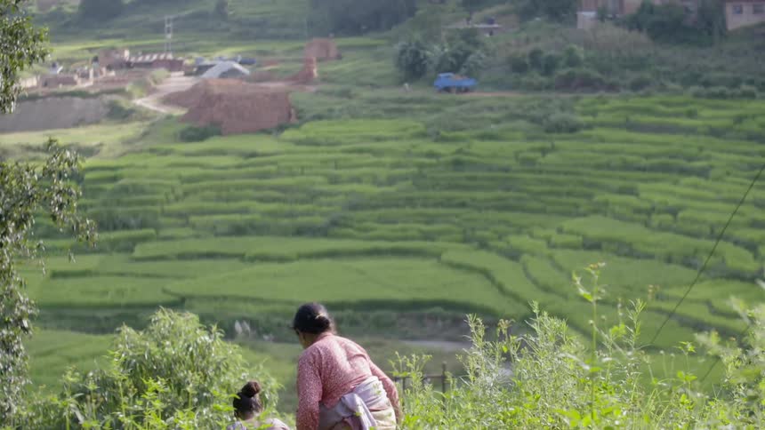 Two women climb down a bush covered hill