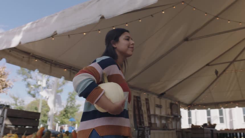 Brunette woman with a sweater a bag and jeans picks a pumpkin to purchase in the market