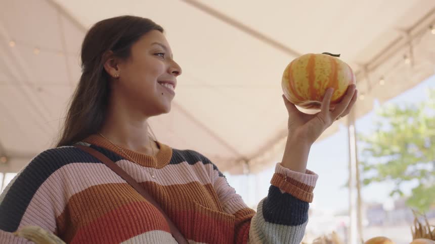 Brunette woman with straight hair and a sweater choose a pumpkin to buy in the market