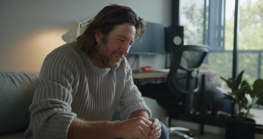 Man smiles while talking on a video call through a laptop at home