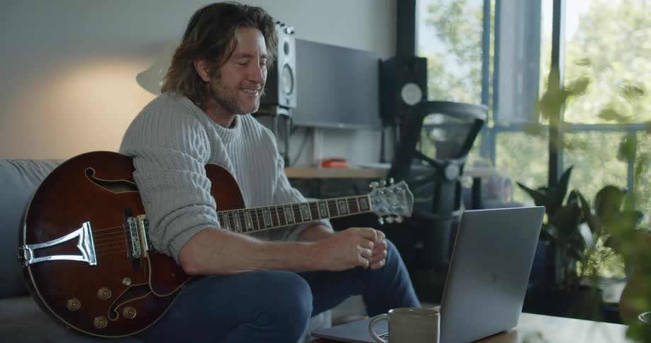 Man holding guitar and sitting on sofa waves goodbye and blows kiss before ending video call