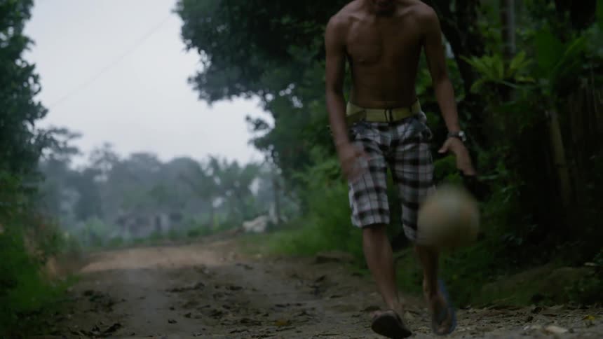 Man dribbling a ball through his legs and down a dirt road