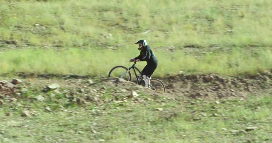 A person rides a bike outdoors on a dirt path near trees and surrounded by grass during the day