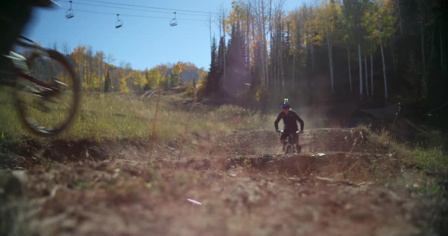 Two cyclists riding mountain bikes on a dirt road on the hills next to the forest