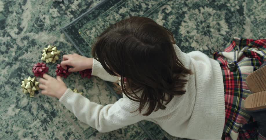 A little girl lays on her stomach on the floor while playing with decorative bows