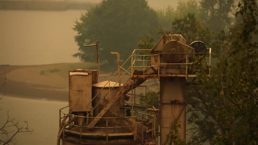 A rusted water tower sits next to a lake