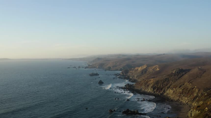 Aerial view of ocean waves crashing on the coastal hills