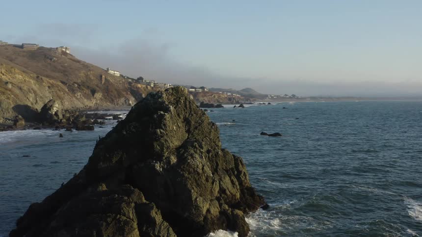 Mountains against the ocean with small structures on the side overlooking the water with hazy skies