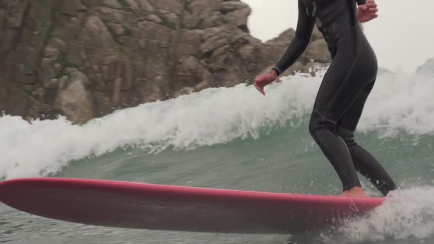 A female surfer catches waves on a rocky coast