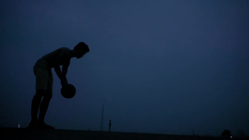 A man is dribbling a basketball in a dark area