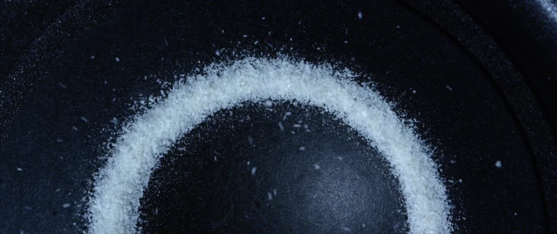 White crystalline granules are bounced atop a dark vibrating surface