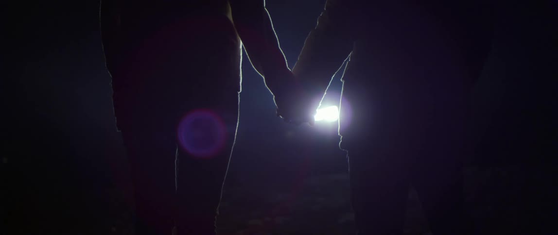 Two people are standing and holding hands in front of a bright light