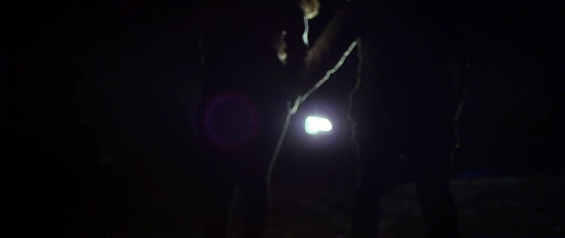 Couple wearing coats and holding hands run toward parked vehicle with lit headlights at night