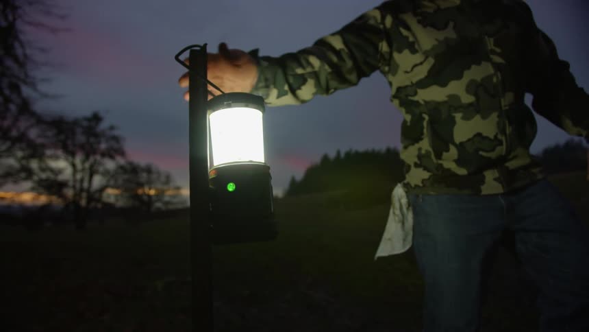 A man with a hat walking up and taking a lantern from a post with the sky and clouds in the background