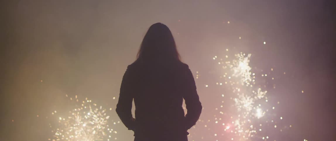 A woman stands outside watching fireworks at night