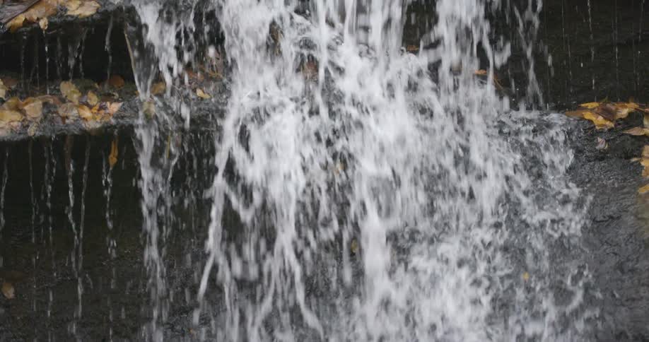 A waterfall over rock or slate with leaves during the day