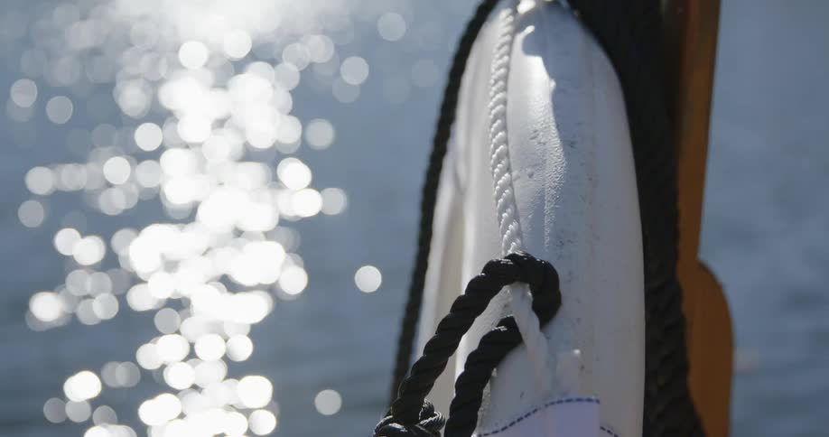 A white life ring with black rope hangs on a deck next to a lake