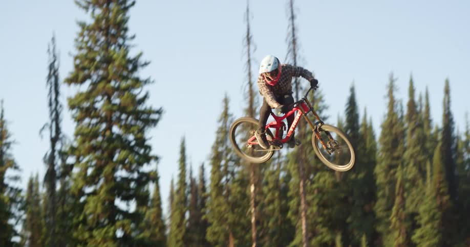 Man riding a bike hops up into the air over a slope performs a stunt and then lands it in a forest at daytime