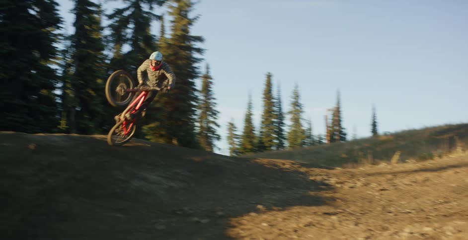 A cyclist jumps over a large dirt mound in a forest