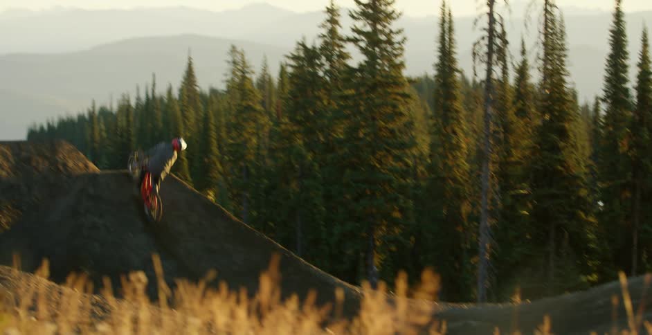 Cyclist driving a bicycle on a track jumps over dirt ramps near the pine forest on the mountain