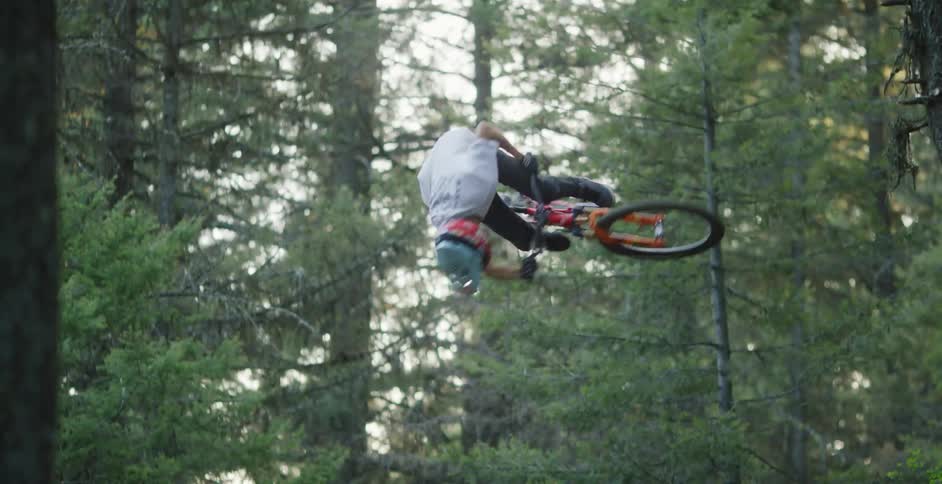 A teenager on a bicycle does tricks on tall mounds of dirt in a forest