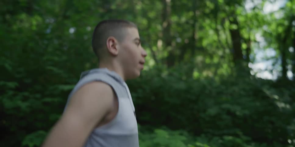 Teenage boy with cerebral palsy walking over the lawn next to the forest