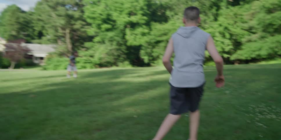 A boy kicks a soccer ball in a grass field at daytime over to a teenage boy who limps over to the ball